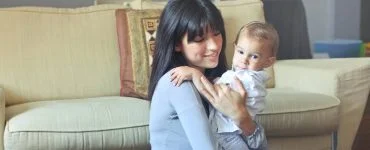 woman in gray sweater carrying toddler in white button up shirt