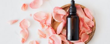 composition of cosmetic bottle with pink rose petals and wooden plate