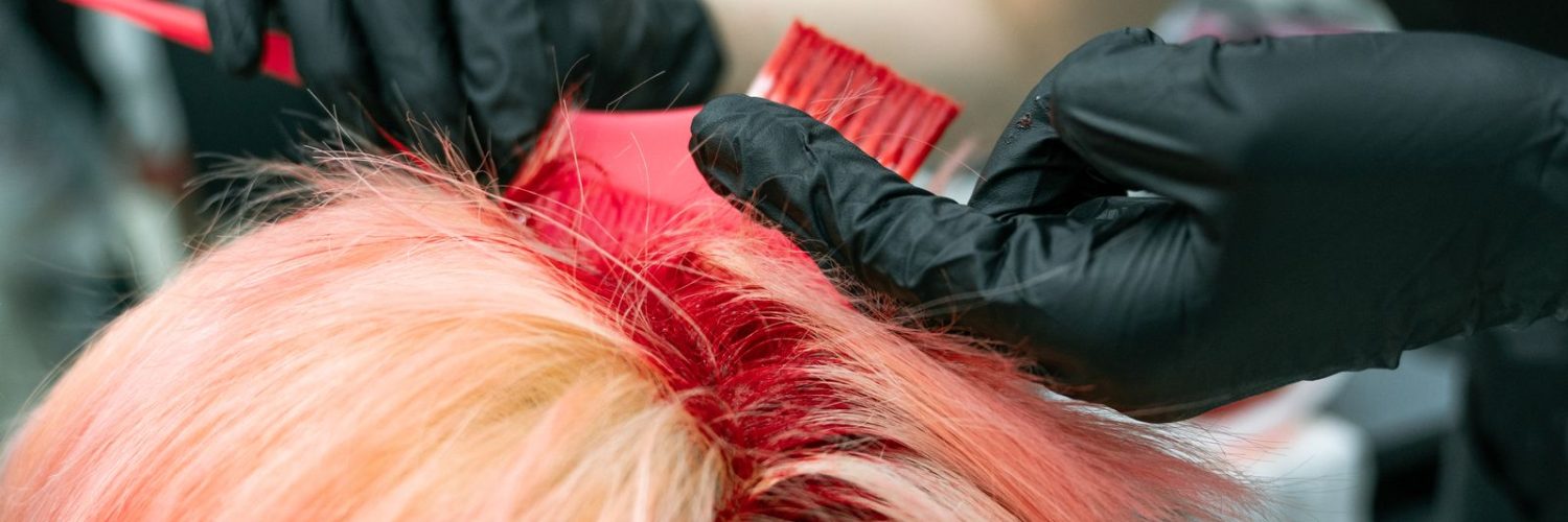 Handen met handschoenen brengen haarverf aan op een lok haar tijdens het kleuren