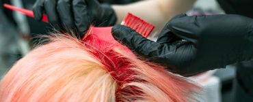 Handen met handschoenen brengen haarverf aan op een lok haar tijdens het kleuren