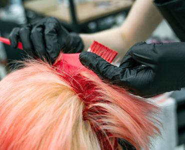 Handen met handschoenen brengen haarverf aan op een lok haar tijdens het kleuren