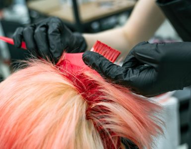 Handen met handschoenen brengen haarverf aan op een lok haar tijdens het kleuren