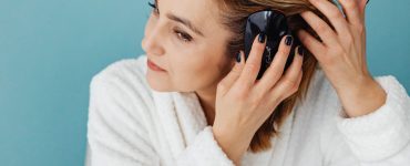 Vrouw in witte badjas borstelt haar lange haar voor de spiegel als onderdeel van haar haarverzorging