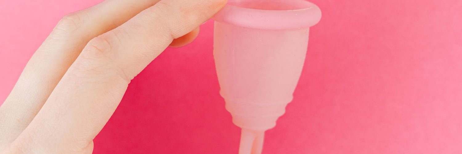 Hand met een roze menstruatiecup, een alternatief voor een inlegkruisje als je ongesteld gaat zwemmen