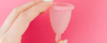 Hand met een roze menstruatiecup, een alternatief voor een inlegkruisje als je ongesteld gaat zwemmen