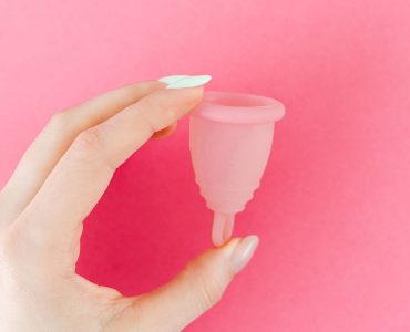 Hand met een roze menstruatiecup, een alternatief voor een inlegkruisje als je ongesteld gaat zwemmen